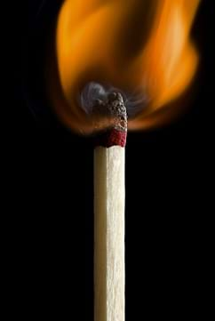 A closeup photograph shows a burning match with an orange flame.