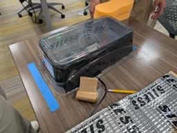 A photo of two students sitting at a table, examining a breadboard and other project materials.
