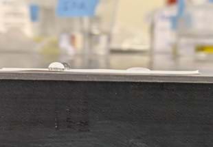 A photo showing a close-up of two pure water droplets and one soapy water droplet on a strip of Teflon tape. 