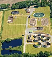 An aerial photograph shows some acreage of land with trees, ponds, buildings and roads as well as many constructed round and oval concrete pond structures.