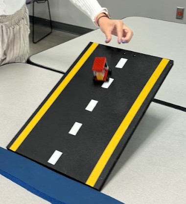 A photo of a student sending a completed plastic brick car down the ramp test. 