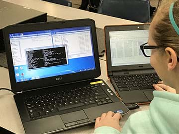 Young female with glasses looking at two laptop computers, analyzing exif metadata.