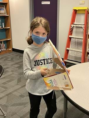 An image of a student with a harp made of cardboard and string.