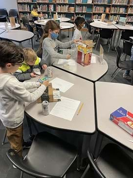 An image of students working their plan using the recycled materials. Some students are cutting and some students are taping.