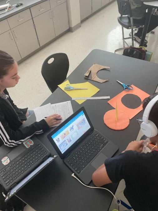 Two students check to see whether their sundial works by observing where the shadow falls after light is shined on it. 