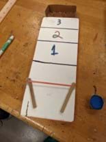 Student prototype with score numbers written on the board. The puck launch mechanism is made of a stretched rubber band like a slingshot.