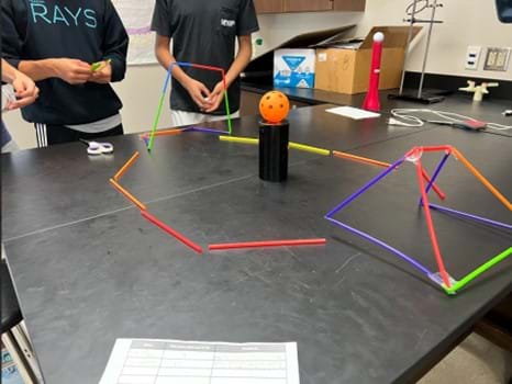 A photo showing a student-created game with a structure made out of straws and a wiffle ball in the center.