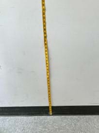 A photo showing a tape measure taped to the wall. The bottom of the tape measure is on the ground.