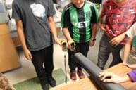 A photo of three students standing in front of a leaf blower holding two anemometers.