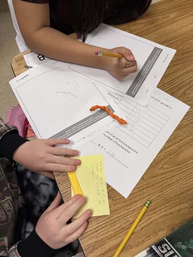 A photo of a student desk showing 2 sets of student hands working. One student is holding a pencil and writing on the planning worksheet, while the other student is folding tissue paper. There is another piece of tissue paper that has already been folded laying on the desk. A photo of a student desk showing 2 sets of student hands working. One student is holding a pencil and writing on the planning worksheet, while the other student is folding tissue paper. There is another piece of tissue paper that has already been folded laying on the desk.