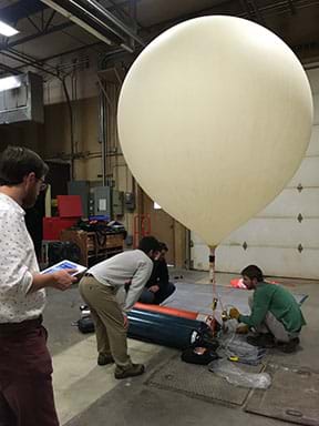 Photograph showing participants filling the large latex high-altitude balloon inside of a large garage building.