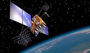 A colorful artist's rendition shows a GPS satellite in orbit. The satellite is adorned with solar panels for generating electricity and has a metallic core with various instruments surrounding the main body.