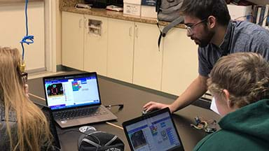 This image shows students sitting at a table with their laptop computers learning some basics of this lesson and its associated three-part activity.