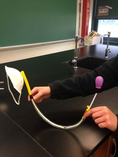 A catheter prototype on display from a student. The student compares the delivery system size to an N95 mask.