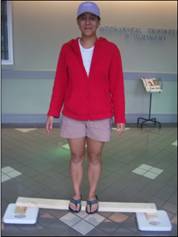 Photo of a person standing on a wooden beam that is supported by two blocks, which are placed over two scales under each end of the beam. 