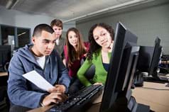 Photo shows four teenagers gathered around a computer monitor.