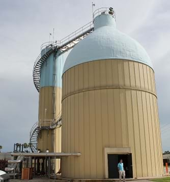 A photo shows a man standing near two domed structures, one narrow, one wide, both more than 50-feet high.