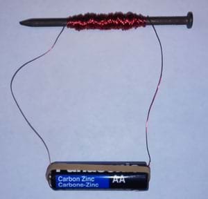 Photo shows copper wire wound around an iron nail and hooked to the ends of an AA battery with a rubber band.