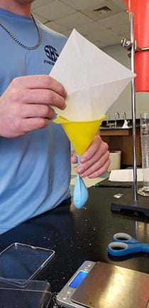 A student loading a balloon sample while holding necks and of both the funnel and the balloon.