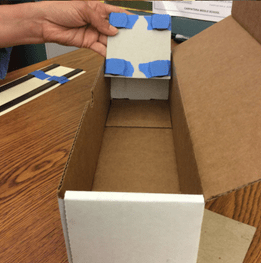 A photo showing an example maglev train device, with four disk magnets taped to the corners of a square piece of cardboard.
