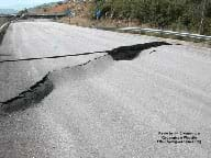 Photo shows a long stretch of highway with a upraised bump and crack in the asphalt across the width of the road in the foreground.