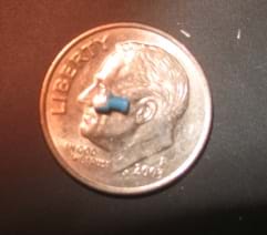 A tiny plastic blue tube device sits on a dime, showing its size.