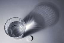 Photo shows a glass containing a clear liquid and a chalk tablet sitting next to it.