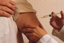 Photo shows hands injecting a syringe into a man's upper arm. 