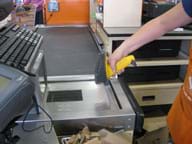 Photo shows a person using a handheld barcode scanner at a store check-out stand.