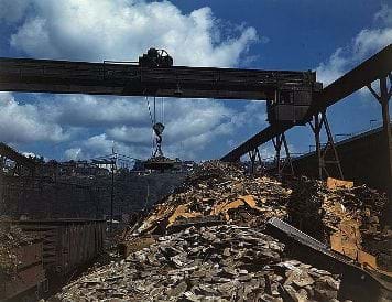 A photograph shows carloads of scrap metal being sorted and moved at the Allegheny Ludlum Steel Corp.'s steel mill in Pennsylvania in the 1940s. An overhead magnet deposits the scrap in a loader that carries it to a furnace to be melted down for re-use.