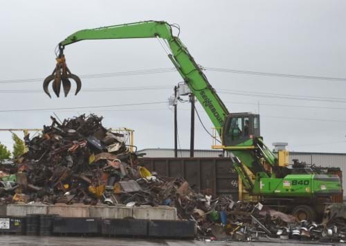 A crane's claw is positioned above a pile of scrap metal.