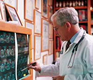 Photograph shows a man in a white coat looking at films (results) from an MRI.