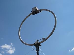 A photograph shows a shortwave loop antenna with attached tuner units, which looks like a 2-meter circle of metal on a pole with other small attached devices and wires.