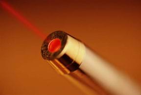 Photo shows the end of a metal tube with a red beam of light extending from it.