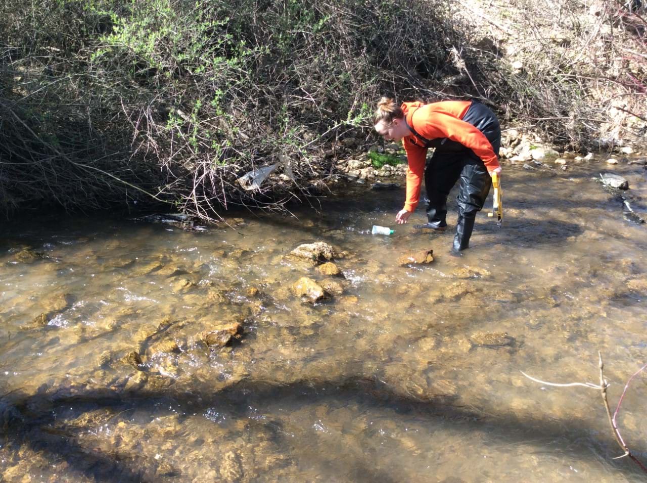 Two students stand in a stream and use measuring tape in a flow rate exercise. 