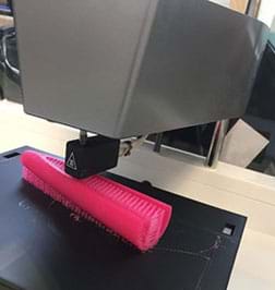 A photograph shows a 3D printer in action, layering down a polymer material in a computer-specified pattern to create an object.