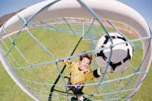 A soccer goalie reaches for a black and white ball caught in a net.