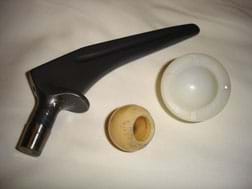 A photograph shows three objects: a hip bone-shaped dark metal item, a hard white spherical object that looks like a portion of a hard-boiled egg white, and a yellowish plastic sphere with its centered drilled out from one side.