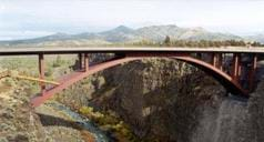 Landscape photo shows an arched metal bridge over a river gorge.