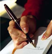 Photograph shows a hand holding an ink pen and writing on paper.