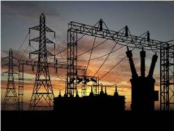 A silouette of a power station and two large transformer towers connected by wires, against a background of a sunset sky.