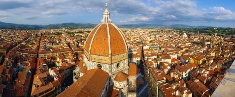 A wide photograph of the view from the top of Giotto's Campanile shows the various terracotta roof top shapes in Florence, Italy.