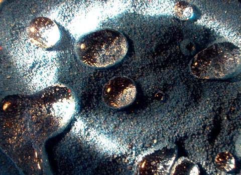 Spherical droplets of water sit atop a surface of fine sand grains.