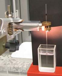 Photo shows a glass tube held from above and positioned vertically into a container of water below it. Photo shows a glass tube held from above and positioned vertically into a container of water below it.